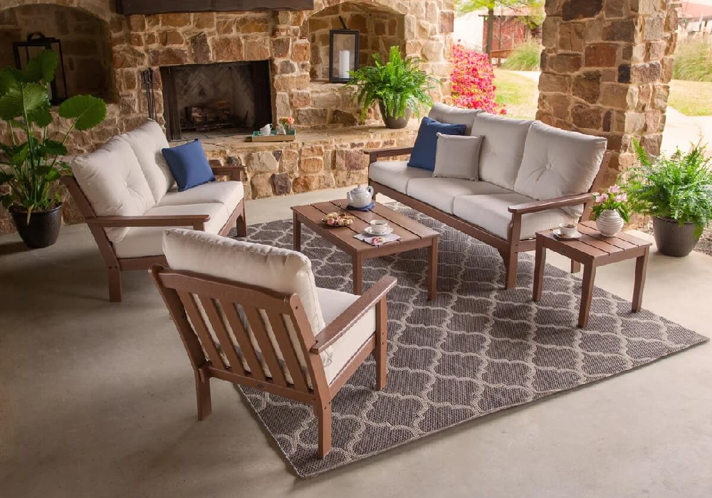 Commercial deep seating furniture arranged around a coffee table in a covered outdoor lounge with a stone fireplace.